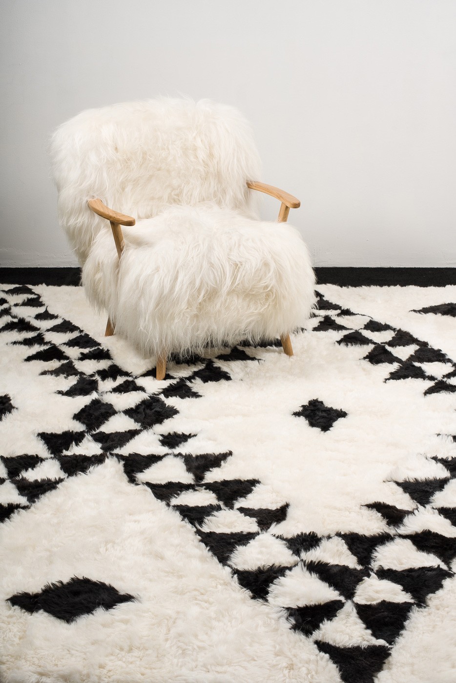 Notre fauteuil Alpina en mouton blanc poils longs et chêne massif est posé sur notre tapis Berbère en mouton noir et blanc. Une décoration d'intérieur adaptée à tous vos intérieurs.