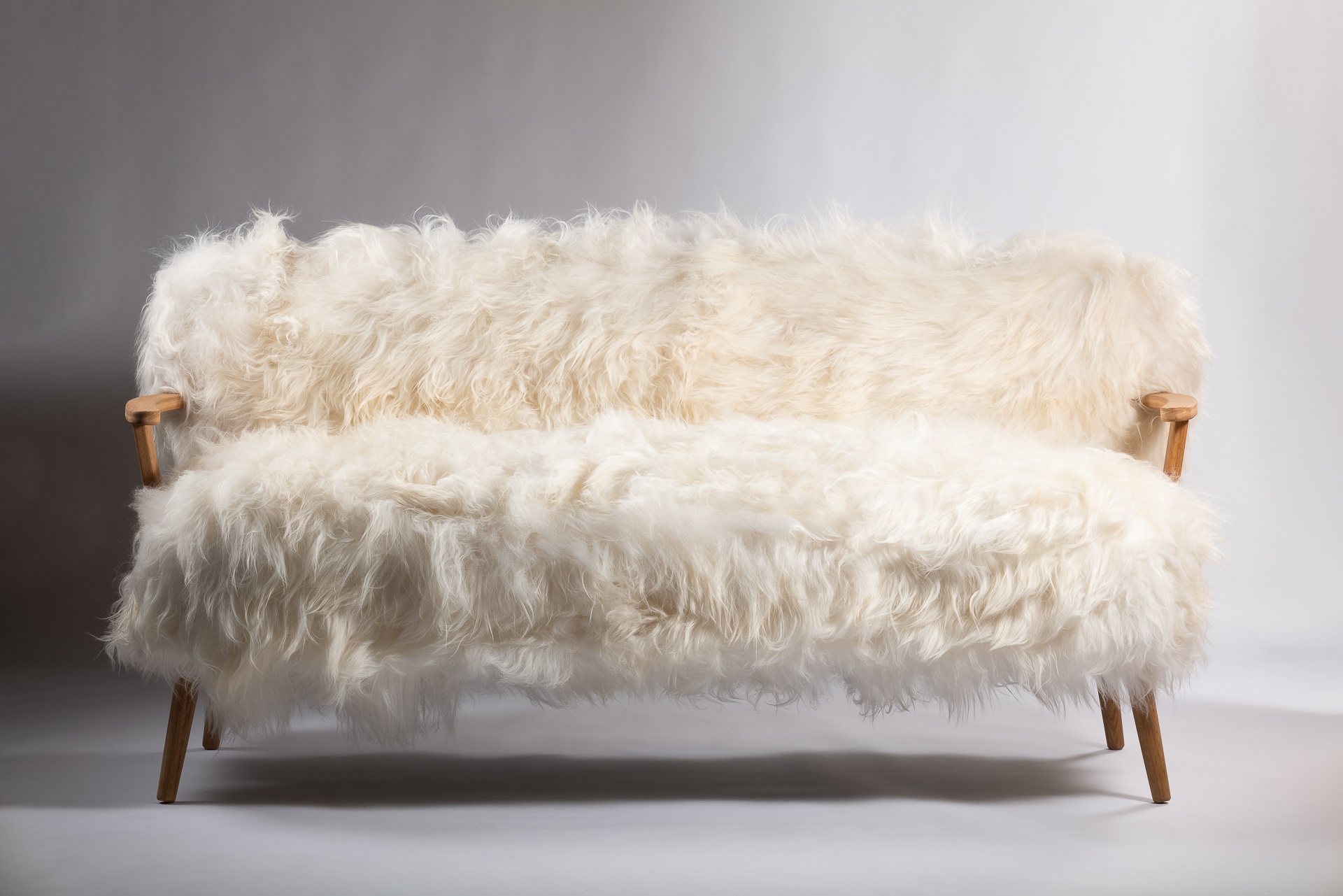 Sofa Alpina : confort luxueux avec un revêtement en mouton, pour des moments de détente inoubliables. Les pieds et les accoudoirs en chêne ajoutent une touche d'élégance naturelle