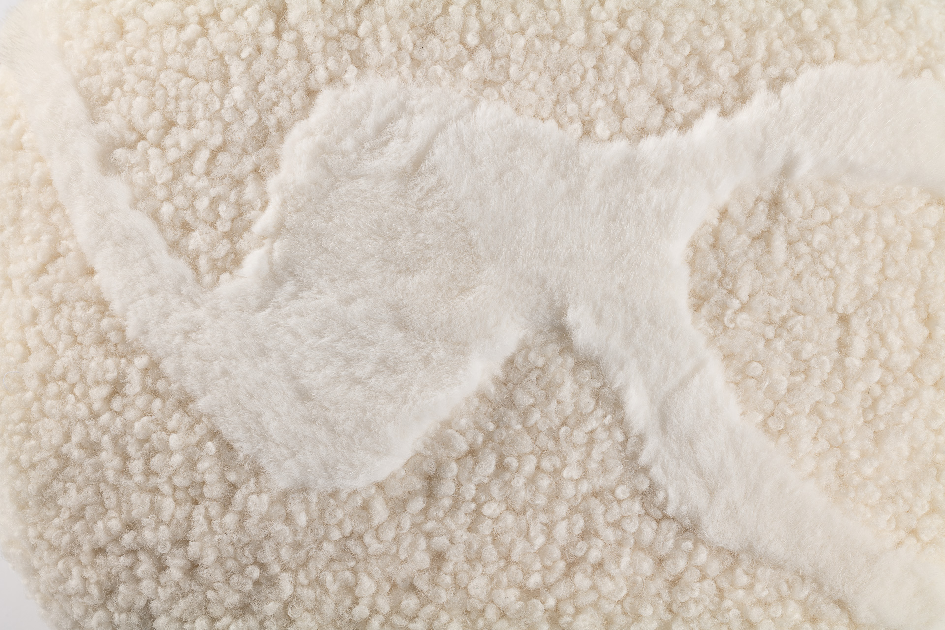 Un coussin rond blanc bi matière luxueuse. Agneau curly et lapin rex blanc forment un motif léger et organique.